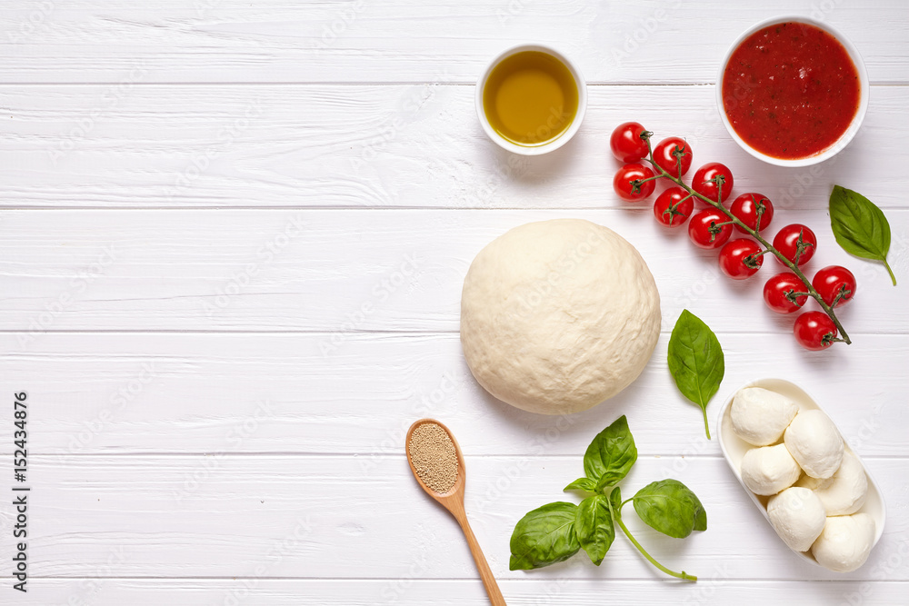Pizza margherita traditional preparation recipe with baking ingridients: raw dough, cherry tomatoes, basil, tomato sauce and olive oil