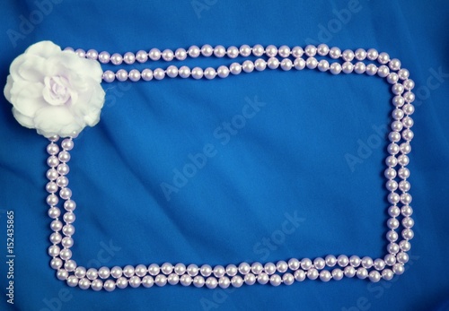 White textile rose bloom and pearls beads frame and blue empty background, bridal texture