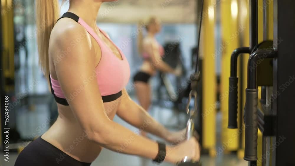 Beautiful girl doing pull-down exercise for upper body, reflection in mirror Beautiful girl doing pull-down exercise for upper body, reflection in mirror