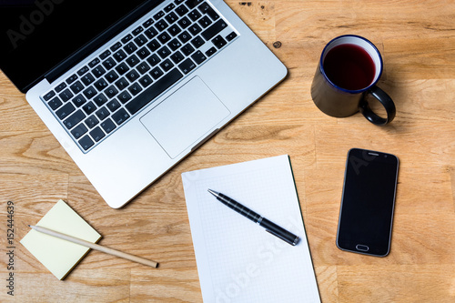 Work environment with a laptop, smartphone, notepad and other accessories on wooden table in a very accurate order. It is seen from above