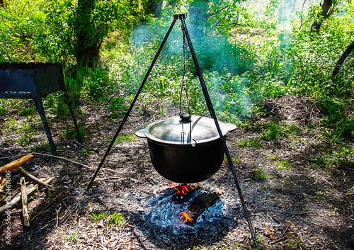 a pot hanging on a tripod over a campfire . blurred background