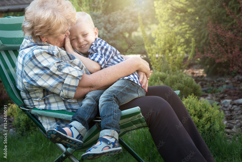 Fototapeta premium Little boy sitting on the arms of his beloved grandmother.Kisses and gentle hugs.Weekend in a country house.