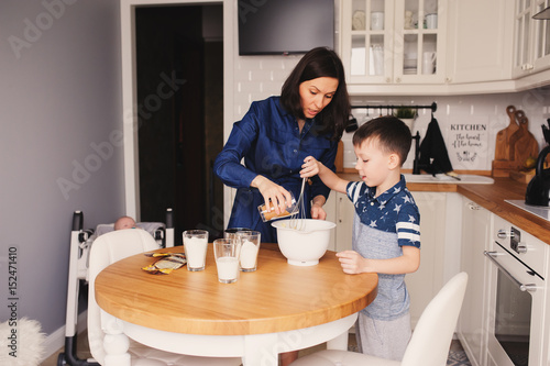 Kid boy helps mother to cook in modern white kitchen. Happy family in cozy weekend morning at home