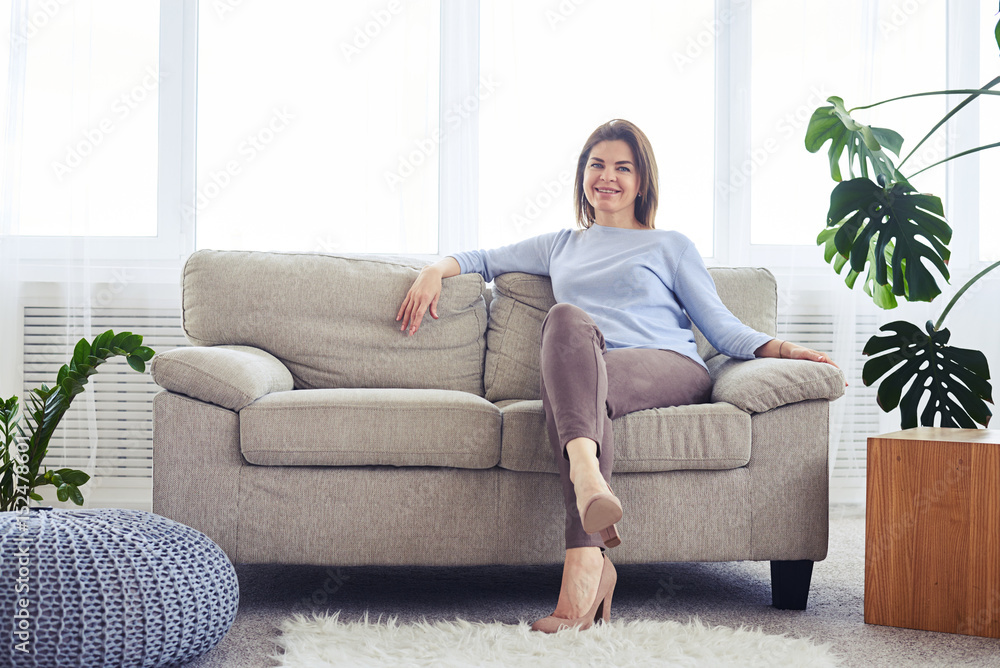 Woman in fashionable clothes sitting on sofa in bright living room Woman in fashionable clothes sitting on sofa in bright living room