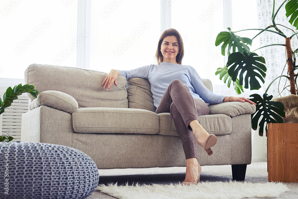 Cheerful brunette having rest on sofa in bright living room Cheerful brunette having rest on sofa in bright living room