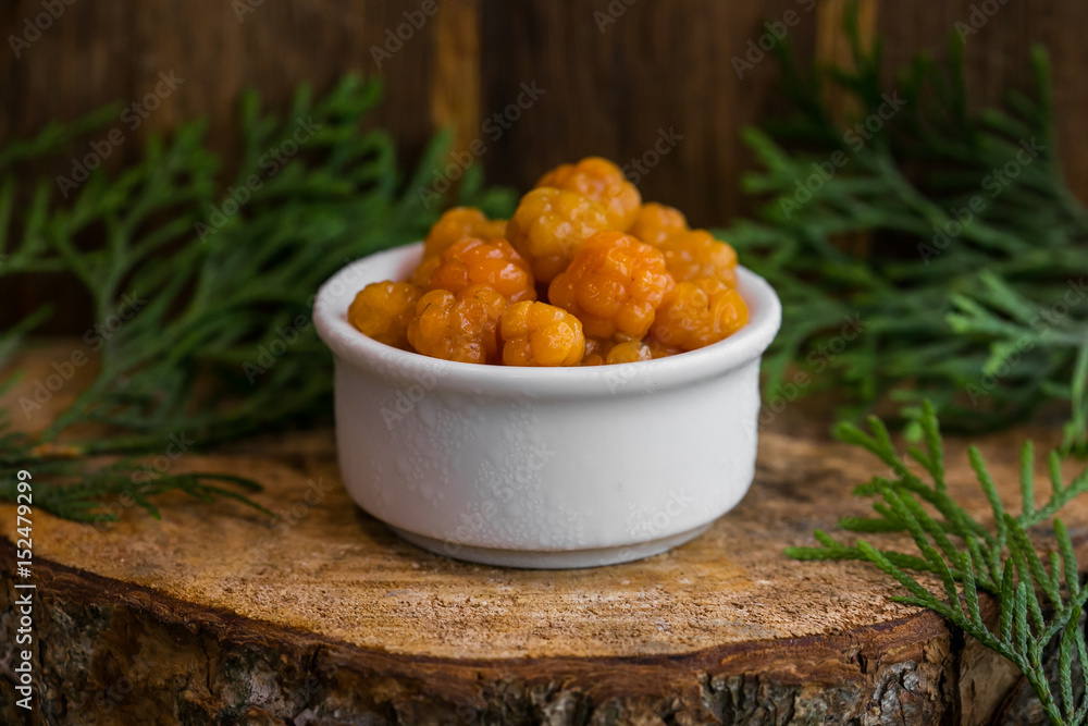 Pickled Cloudberries in a sweet syrup in a white bowl on the wooden background with the leaves of juniper Pickled Cloudberries in a sweet syrup in a white bowl on the wooden background with the leaves of juniper