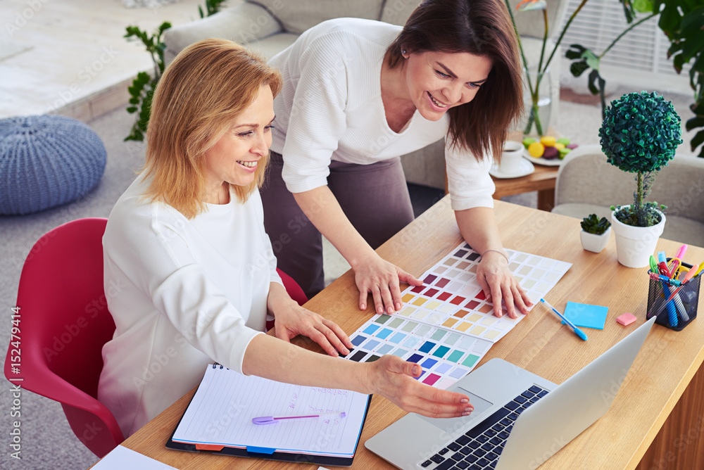 Fototapeta premium Smiling females working with catalog of color palette and laptop