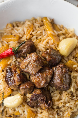 Uzbek Pilaf - Rice with Meat and Vegetables on the table. Pilaf with lamb and garlic zira. close up