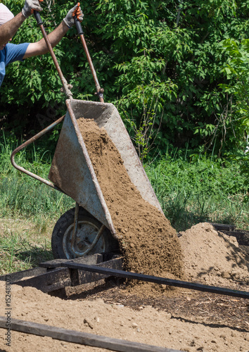 The man pours out the clay from the wheelbarrow