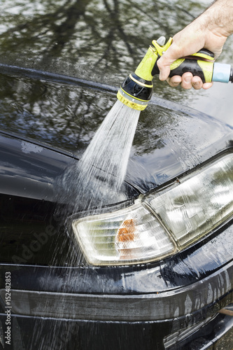 Spłukiwanie karoserii samochodu wodą z węża ogrodowego. Mycie samochodu. Mężczyzna spłukuje samochód trzymając końcówkę węża ogrodowego
