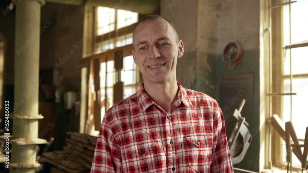 Middle-aged Caucasian male worker in plaid red shirt standing in joinery and looking at camera smiling in slowmotion Middle-aged Caucasian male worker in plaid red shirt standing in joinery and looking at camera smiling in slowmotion