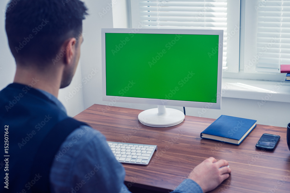 Young man office worker sitting at his desk working at computer with Chromakey on monitor. Office concept with working environment