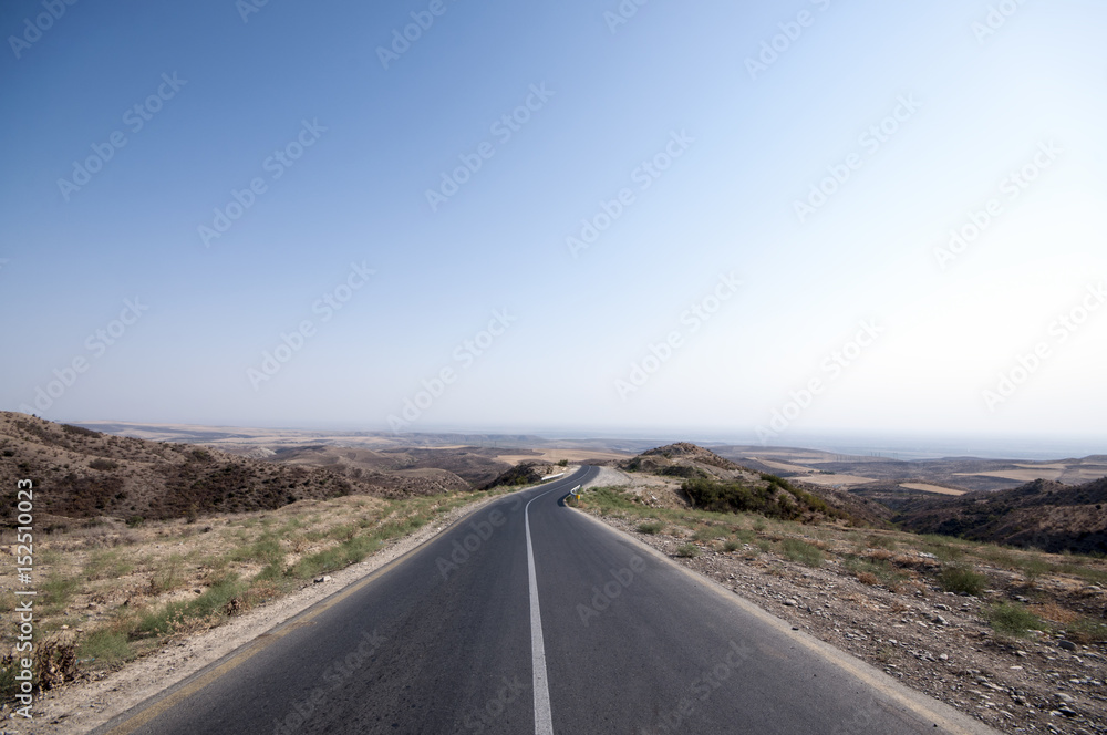 Road vanishing to the horizon under sun rays coming down trough the dramatic stormy clouds. Sunset at the mountain road. Azerbaijan, Ganja