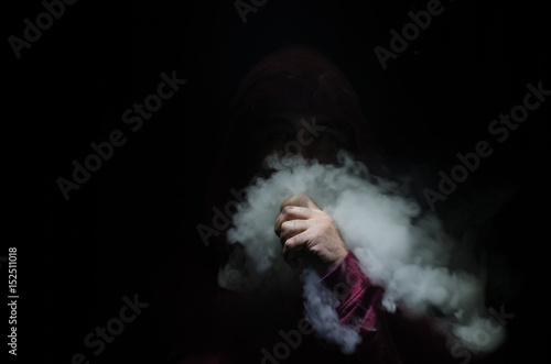 Vaping man holding a mod. A cloud of vapor. Black background. Vaping an electronic cigarette with a lot of smoke