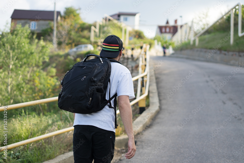 Stylish young man with a backpack walks alone on a mountain road up the slope