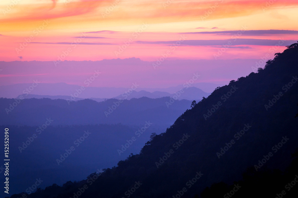 Silhouettes of the mountain hills layer in the morning mist. Colorful summer scene.