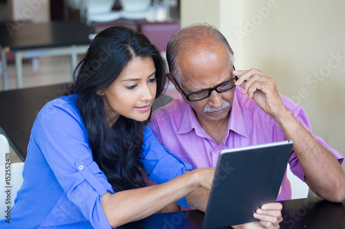 Closeup portrait, sitting young woman showing elderly with black glasses to use portable device,scrutinizing data with great concern, isolated indoors background