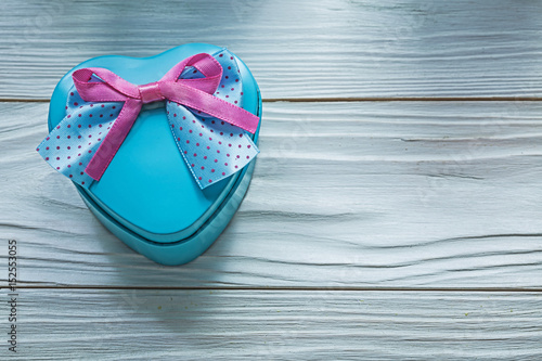 Heart-shaped blue gift box with pink bow on wooden board holiday