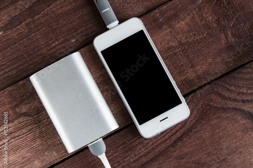 Grey phone and power bank connected by cord on wooden desk