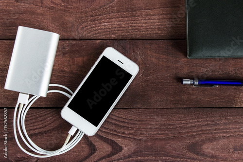 Grey phone and power bank connected by cord with pen and notebook