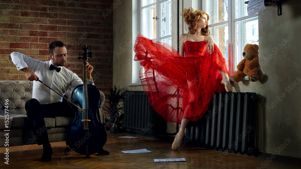 Fototapeta premium Caucasian handsome cellist visits the muse from fairytale in red dress
