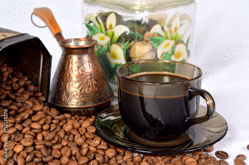 Красивая чашка с кофе и медная турка на рассыпанных кофейных зернах. 
