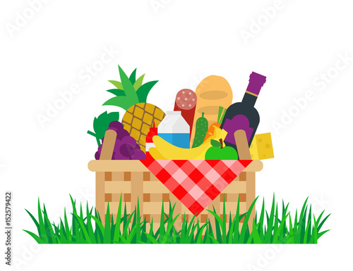 wicker picnic basket with food products on green grass