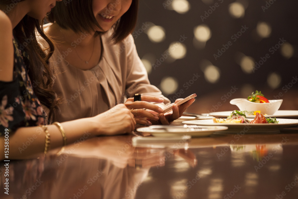 Women are laughing at the bar watching smartphone Women are laughing at the bar watching smartphone