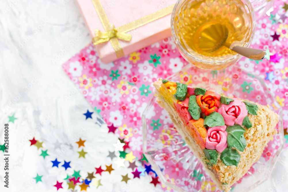 Piece of birthday cake, tea in cup, gift box and colorful confetti Piece of birthday cake, tea in cup, gift box and colorful confetti