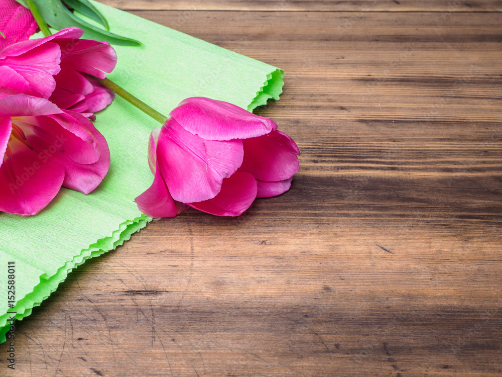 Pink tulips, floral arrangement on wooden background with green paper and space for message. Background for Mother's Day, 8 March and other greeting cards or invitations for lovely women. Soft focus.