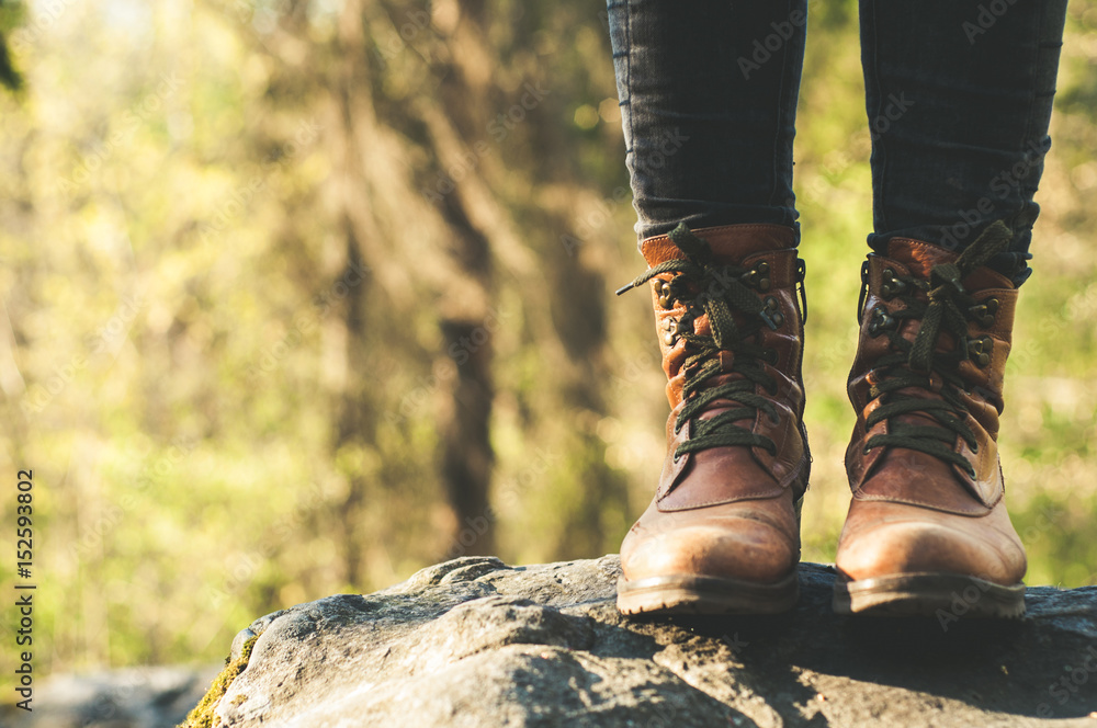 Female legs shod in Hiking boots on the forest background. Travel concept Female legs shod in Hiking boots on the forest background. Travel concept