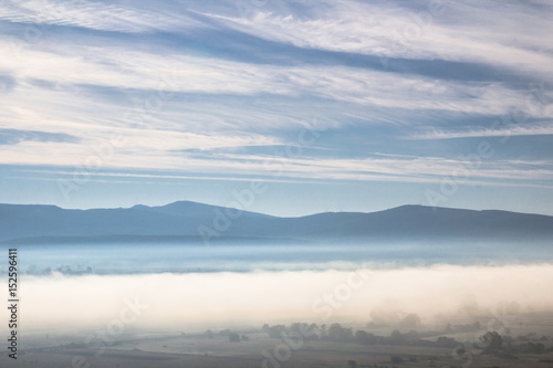Beautiful morning atmosphere in a valley surrounded by hills with a magic mist full of bright light and white cloud and blue sky