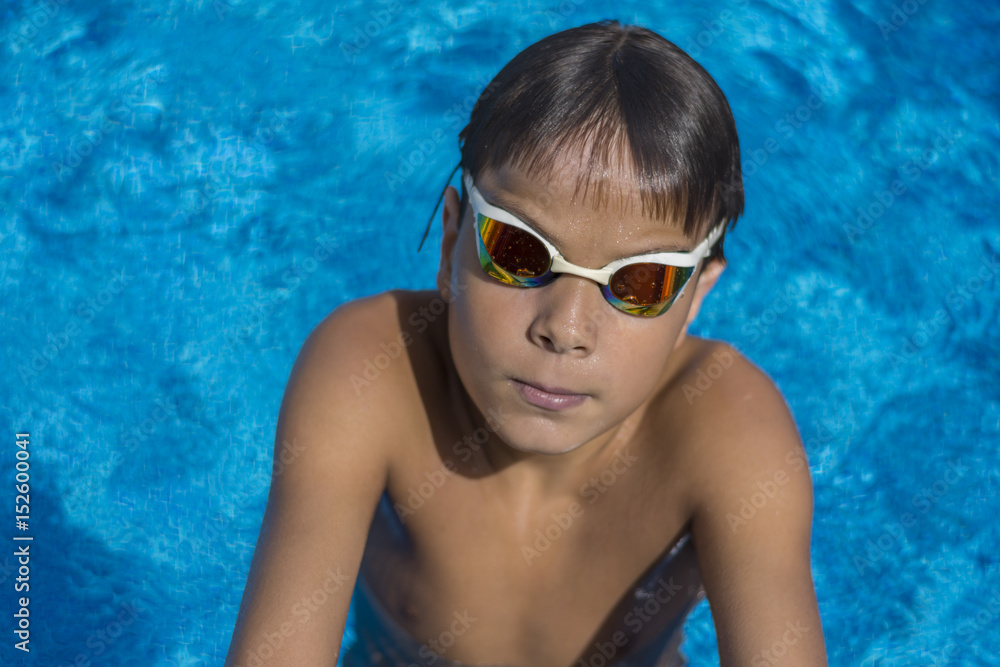 Boy with swimming goggles in pool, above view. Blue water background.