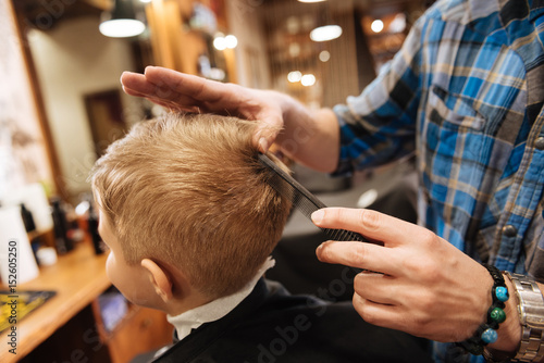 Nice pleasant barber combing the boys hair