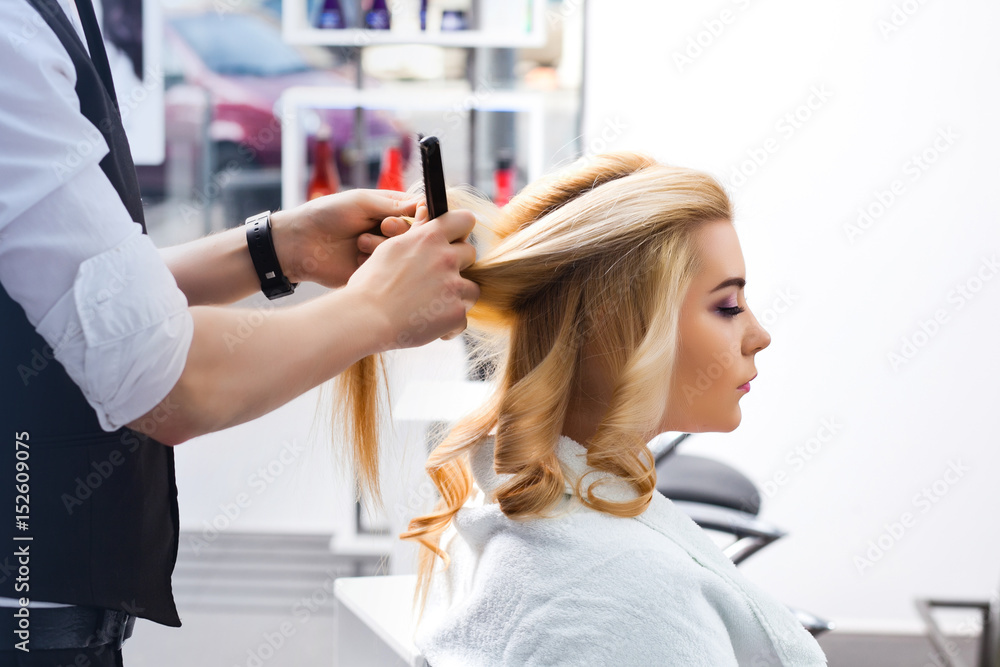handsome Hairdresser does a hairstyle for a blonde girl in a beauty salon handsome Hairdresser does a hairstyle for a blonde girl in a beauty salon