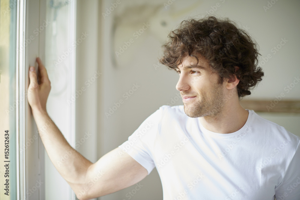 Confident young man portrait. Shot of happy young man standing in living room at the window. Confident young man portrait. Shot of happy young man standing in living room at the window.