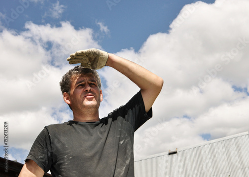 Builder looks up,  shielding his eyes from the sun