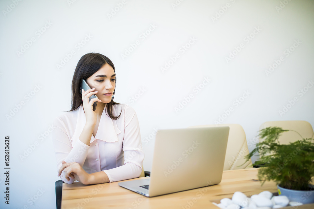 beautiful young business woman sitting at office desk and talking on cell phone beautiful young business woman sitting at office desk and talking on cell phone