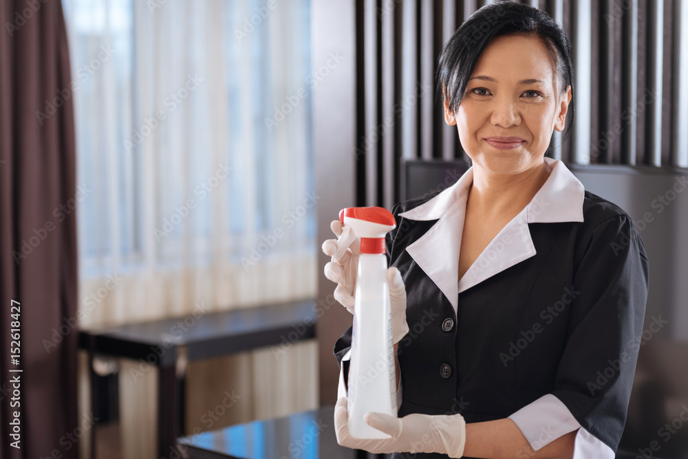 Positive Asian hotel maid holding a cleansing agent Positive Asian hotel maid holding a cleansing agent