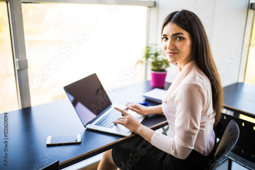 Young beautiful woman using her laptop while sitting in chair at her working place