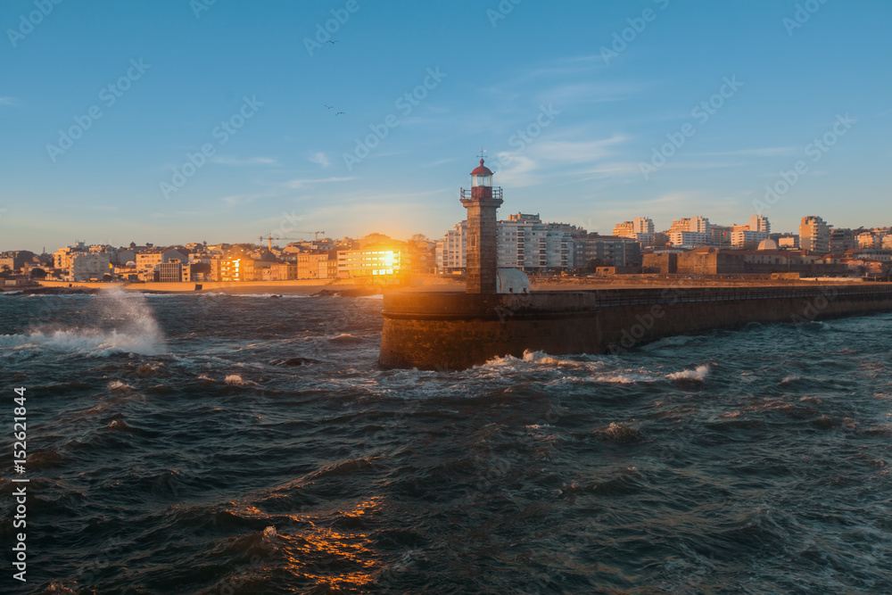 Pier with a lighthouse in the ocean surf during sunset. Porto, Portugal.
