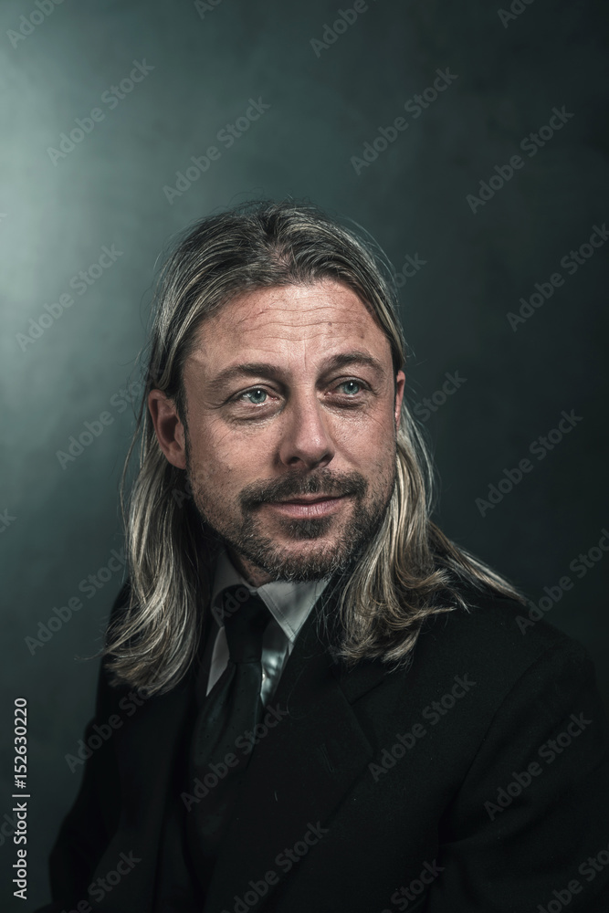Smiling retro victorian style man with blond long hair and beard. Wearing black suit and tie. Smiling retro victorian style man with blond long hair and beard. Wearing black suit and tie.