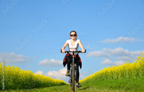 Girl riding a bike on a dirt road in rapeseed field.