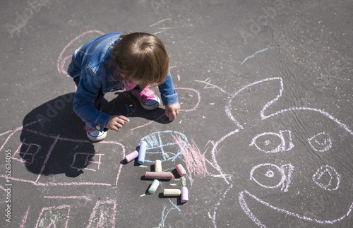 girl in a jeans jacket draws with colored chalks