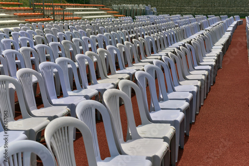 Rows of white folding chairs on lawn before a graduation ceremony in summer time