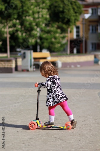 Cute little girl riding a scooter in the summer park, side view