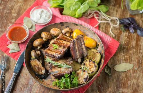 Grilled ribs with mushrooms and zucchini in a frying pan on a table