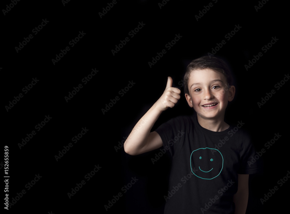 Low key portrait of smiling young boy isolated on black background. Plenty of space left for copy. Hand drawn Smiley face on T-shirt Low key portrait of smiling young boy isolated on black background. Plenty of space left for copy. Hand drawn Smiley face on T-shirt