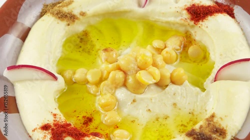 Plate with hummus made in restaurant, appetizer made from mashed chickpeas dip with tahini, lemon, garlic, olive oil, decorated with radish slices and spices
