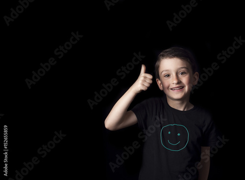 Low key portrait of smiling young boy isolated on black background. Plenty of space left for copy. Hand drawn Smiley face on T-shirt